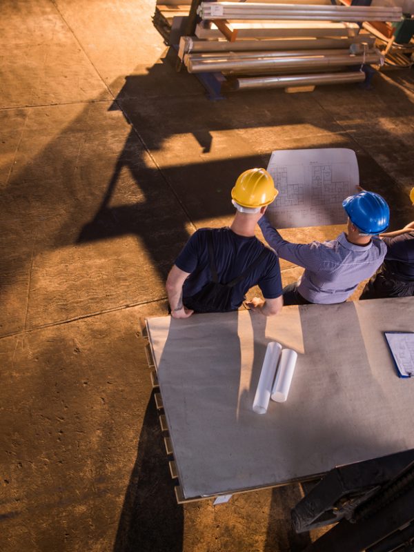 High angle view of inspector examining business plans with two manual workers in a factory. Copy space.